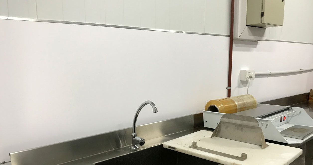 Pared revestida con placas Plastixe blancas junto a una mesada de acero inoxidable