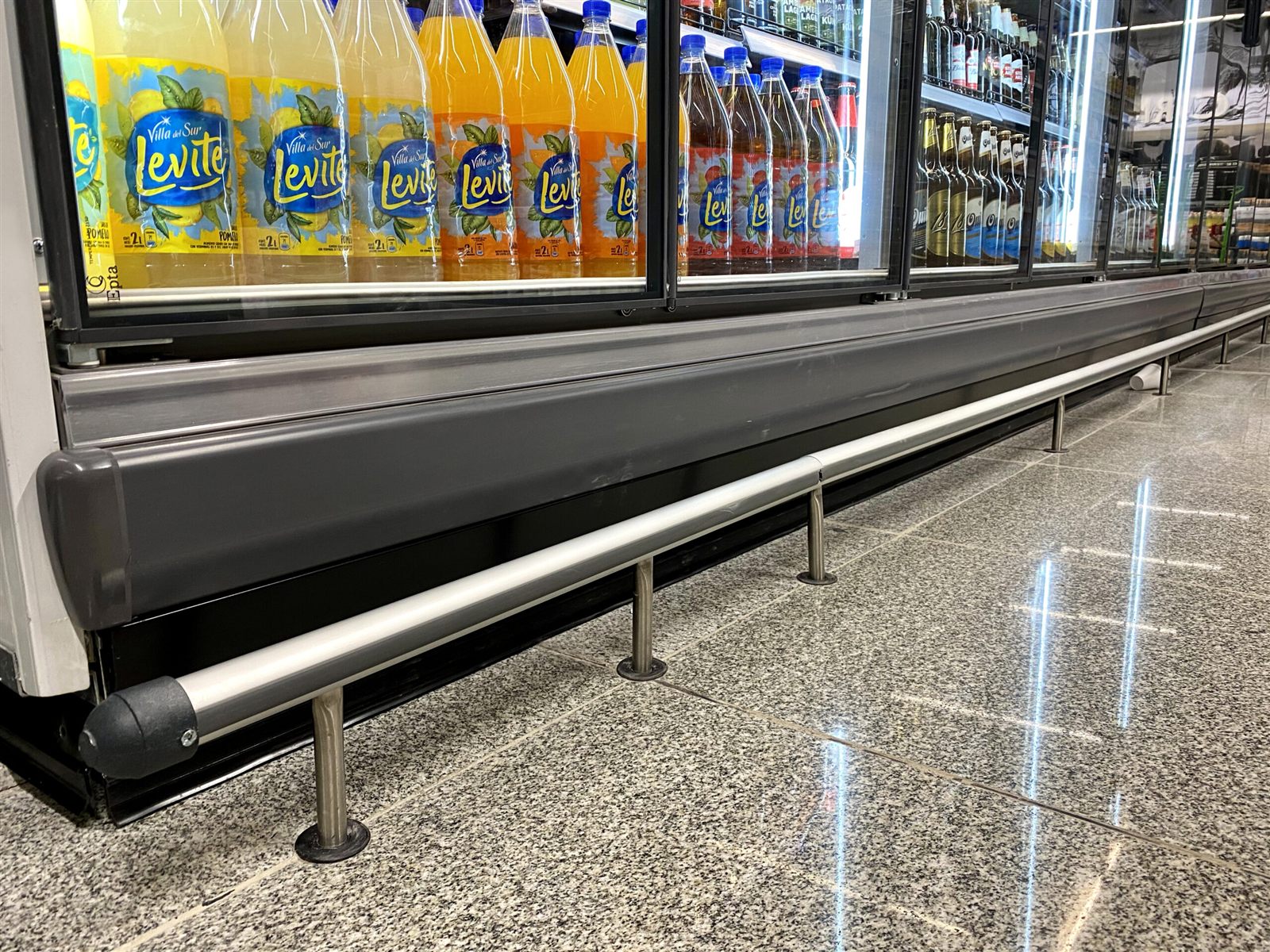 Defensa tubular de acero frente a una heladera de bebidas en un supermercado